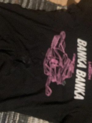 Svart t-shirt med rosa tryck - Säljer en svart t-shirt med ett stort rosa grafiskt tryck av en bil och texten 'BANKA BANKA' i vitt framtill. T-shirten har rund hals och korta ärmar, perfekt för dig som gillar streetwear och coola prints.