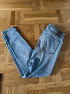 Replay jeans - Säljer ett par ljusblå slim jeans från Replay med klassisk femficksdesign och patch på bakfickan. Jeansen har slitningar och en lagad detalj på ena benet för en skön look⭐️