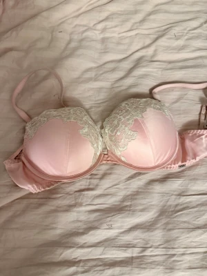 Rosa push-up bh med spets från Lindex - Söt ljusrosa push-up bh från Lindex med vadderade kupor och dekorativ vit spets upptill. Justerbara axelband och hakknäppning bak. Tillverkad i mjukt material för extra komfort och feminin look.