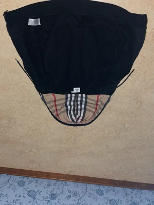 Svart hoodie från Burberry med dragkedja - Snygg svart hoodie från Burberry med klassiskt rutigt foder i huvan och dragkedja framtill. Hoodien har två fickor och justerbar huva med snören. Perfekt för dig som vill ha en stilren och exklusiv look med ikoniska Burberry-detaljer.