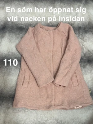 Ljusrosa kappa med fickor - Söt ljusrosa kappa med två snedställda fickor framtill och silkeslen glansig insida. Kappan har en rak passform och stängs med tryckknappar. Perfekt för dig som gillar en stilren och feminin look.🌸 En söm har släppt på insidan vid nacken. Storlek 110