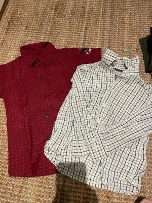 Två skjortor, rutig & vinröd, H&M - Säljer två skjortor: en vit med grönt och blått rutmönster från H&M L.O.G.G. och en vinröd skjorta med små vita prickar och blå knappar. Båda har klassisk krage och knäppning framtill. Perfekta för en stilren look.