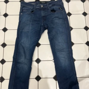 Mörkblå jeans från Replay - Säljer ett par mörkblå jeans från Replay med klassisk femficksmodell och raka ben. Jeansen har snygga slitningar framtill och kontrastsömmar. Perfekta för en avslappnad och trendig look.