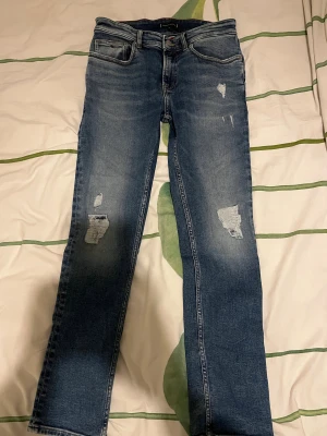 Blå slitna jeans från Tommy Hilfiger🇫🇷 - Snygga blå jeans från Tommy Hilfiger med slitningar och lagom tvättad look. Klassisk femficksmodell, knapp och dragkedja framtill samt bruna läderdetaljer med logga bak. Passar dig som gillar en cool och avslappnad stil.        Köpt för 900kr 💰   Använt ungefär 1-2 gånger men fick exakt samma i present några dagar efter så sen dess har jag bevarat dom fint. Helt nya, inga slitningar eller något negativt✅  Passform👖: passar dig perfekt som är ungefär 170-175cm lång. 