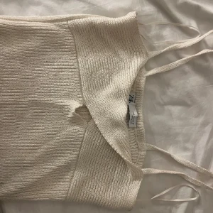 Stickad croppad linnetopp från Zara - Säljer en slutsåld ljusbeige stickad linnetopp från Zara med smala axelband och en snygg cut-out detalj framtill. Toppen är croppad och har en ribbad struktur som ger en cool och trendig look. Perfekt för dig som gillar stilrena och enkla plagg med twist. 
