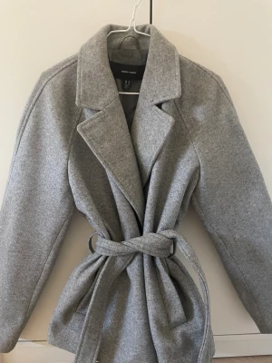 Pris kan diskuteras - Snygg grå kappa från Vero Moda i storlek XS. Modellen har klassisk krage, knytbälte i midjan och raka, långärmade ärmar. Materialet är mjukt och känns som ullmix, perfekt för kyliga dagar. Enkel och stilren design som ger en clean vibe.