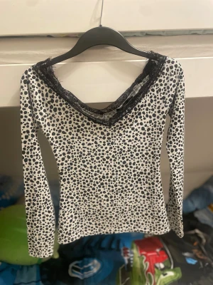 Prickig långarmad topp från Boohoo - Säljer en vit långarmad topp från Boohoo med svarta prickar och snygg svart spets runt halsringningen. Toppen har en smickrande v-ringad form och är tillverkad i ett mjukt, ribbat material. Perfekt för dig som gillar coola detaljer och mönster.