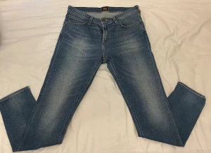 Blå Lee Malone jeans W31 L30 - Säljer ett par klassiska blå Lee Malone jeans med snygg tvätt och raka ben. Jeansen har fem fickor, gul kontrastsöm och Lee-läderpatch baktill. Passar dig som gillar en tidlös look och vill ha jeans med normal passform.
