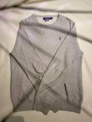  Polo Ralph Lauren tröja  - Snygg grå tröja från Polo Ralph Lauren i mjuk pima bomull. Klassisk rund hals och diskret logga broderad på bröstet. Långärmad med ribbade muddar vid ärmslut och nederkant. Perfekt för dig som gillar stilrena och enkla plagg. Skriv om du har frågor!