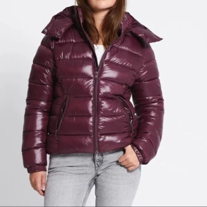 Vinröd pufferjacka med huva - Säljer en snygg vinröd pufferjacka med glansig finish och huva. Jackan är i storlek XL men skulle mer säga att de är en blandning av S/M