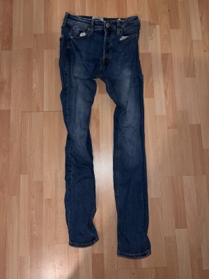 Blå skinny jeans från Jack & Jones - Säljer ett par blå skinny jeans från Jack & Jones med klassisk femficksdesign och snygga slitningar. Jeansen har normal passform i midjan och är tillverkade i mjukt denimtyg med stretch för extra komfort. Perfekt för dig som gillar en smal siluett.