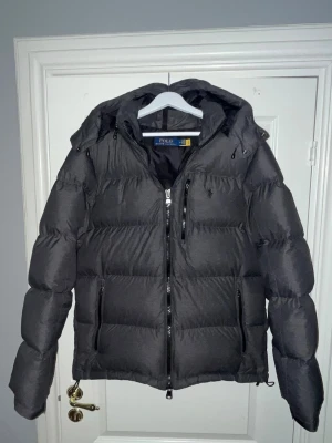 Grå dunjacka från Polo Ralph Lauren - Snygg grå dubjacka från Polo Ralph Lauren med avtagbar huva. Använd fåtal gånger förra vintern.   Qr-koden i nacken visar att jackan är äkta. 