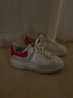 Alexander McQueen vita sneakers med röd häl - Säljer ett par chunky vita sneakers från Alexander McQueen med röd mockadetalj på hälen och logga i silver. Äkta givetvis och använda fåtal gånger