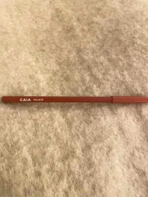 CAIA Mojave läppenna brunröd - Snygg läppenna från CAIA i färgen Mojave, med en varm brunröd ton. Pennan har klassisk trädesign och är spetsig för exakt applicering. Perfekt för att definiera och fylla i läpparna med en naturlig och trendig look.