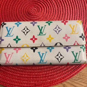 Louis Vuitton multicolor plånbok - Snygg plånbok från Louis Vuitton i vitt skinn med ikoniskt LV-mönster i flera färger. Plånboken har flera kortfack, fönster för ID och dragkedjefack för mynt. Perfekt för dig som vill ha något både klassiskt och färgglatt i väskan.