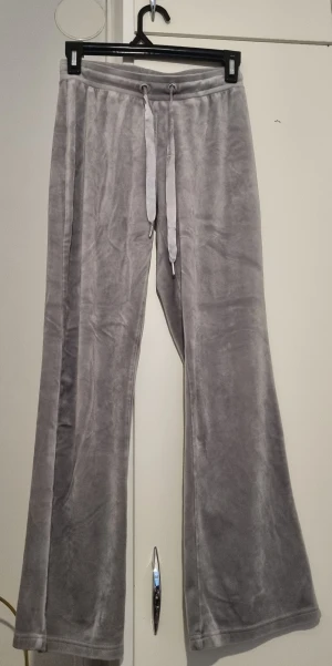 Grå mjukisbyxor med snörning - Supermjuka grå mjukisbyxor med breda ben och snörning i midjan. Materialet är lent och har en lätt glansig finish som ger en chill vibe. Perfekta för att hänga hemma eller när du vill vara extra bekväm. Snyggt loose fit och coolt fall.