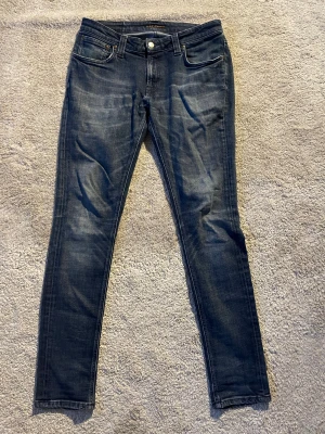 Mörkblå Nudie Jeans Skinny Lin 32/32 - Snygga mörkblå jeans från Nudie Jeans i modellen SkinnyLin. Klassisk femficksdesign med orange sömmar och Nudie-logga på bakfickan. Jeansen har en super snygg wash och är i mycket bra skick.