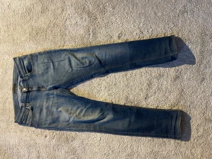 Blå slimfit jeans från nudie. - Snygga blåa jeans med snygg wash från Nudie. Storlek 31/34 men de är ganska små i storleken. De är slitna under gylfen men annars är de i bra skick. Hör av dig vid funderingar😁