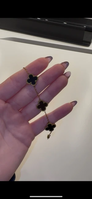 Fyrklöv armband - Superfint armband med fem fyrklöverformade hängen i svart och guldfärgad kedja. Ikonisk design som verkligen sticker ut och ger en lyxig känsla. Perfekt accessoar för dig som gillar klassiska smycken med en modern twist. Rostfri stol