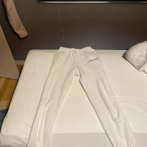 Vita mjukisbyxor  - Vita mjukisbyxor med elastisk midja och snörning. Byxorna har en avslappnad passform och är tillverkade i mjukt material. Finns en logga på ena höften.