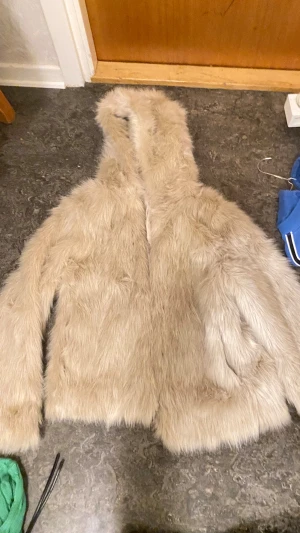Beige pälsjacka med huva från H&M - Säljer en fluffig och snygg beige pälsjacka från H&M Divided i storlek 36. Jackan har huva och är helfodrad med mjukt tyg på insidan. Perfekt för dig som vill ha en statement piece med extra cozy vibe. Jackan har långärmade ärmar och en loose passform.