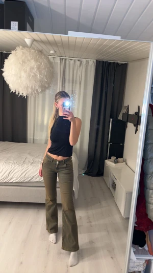 Bootcut jeans i olivgrönt från Nelly - Snygga olivgröna bootcut jeans från Nelly med låg midja och klassiska fickor med lock och knapp bak. Jeansen har en lätt tvättad look och är tillverkade i stretchigt denim för skön passform. Perfekt för dig som gillar retrovibbar och vill sticka ut.