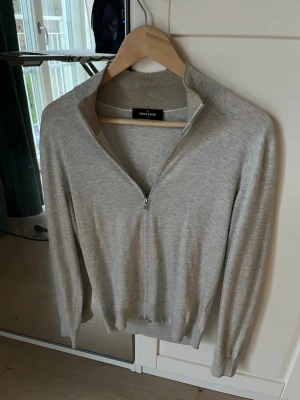 Ljusgrå kofta från Gran Sasso - Snygg ljusgrå kofta från Gran Sasso med stilren design och half zip-dragkedja. Tröjan är stickad i mjuk bomull och har ribbade muddar vid krage, ärmslut och nederkant. Perfekt att slänga på över en t-shirt för en clean look. Storlek 46 vilket motsvarar S
