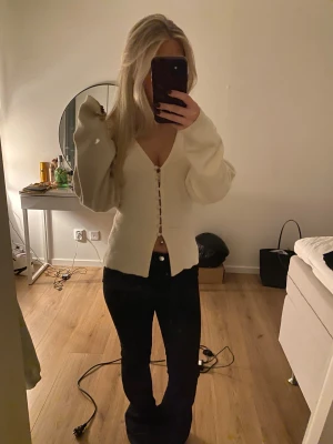 Krämvit kofta med v-ringning och knappar - Superfin krämvit kofta med djup v-ringning och snygga knappar hela vägen framtill. Koftan har långa ärmar och en lite loose passform, perfekt att slänga på sig över ett linne eller t-shirt. Mjuk och skön, passar till allt.