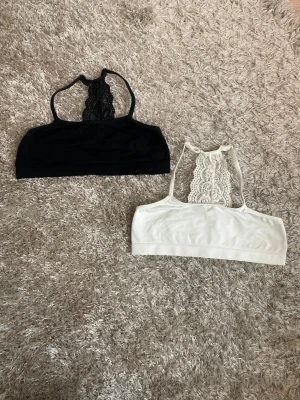 Svart och vit spets topp  - Två toppar i svart och vitt med snygg spetsdetalj i ryggen. Tunn, mjuk och stretchig känsla tack vare polyamid och elastan. Perfekt för dig som gillar stilrena och feminina detaljer. Säljes som ett set! OBS: GÅR ATT SPÄNNA IN!