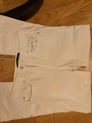 Vita bootcut jeans från Denim Rebel - Snygga vita jeans från Denim Rebel med bootcut-ben och råa, fransiga kanter längst ner. Klassisk femficksmodell med dragkedja och knapp framtill. Materialet är jeans och passformen är normal, perfekt för dig som gillar en clean och stilren look.