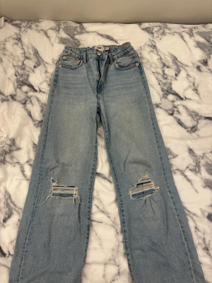 Ljusblå jeans med hål från 157 - Ljusblå vida jeans från lager 157 Boulevard Star med slitna hål på båda knäna. Klassisk femficksmodell, dragkedja och knapp framtill. Jeansen har en avslappnad passform och är tillverkade i denim med snygg tvätt. Säljes pga att de ej används.