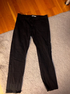 Svarta manchesterbyxor från Calvin Klein - Svarta manchesterbyxor från Calvin Klein med smal passform. Klassisk femficksdesign, CK-logga på bakfickan och dragkedja fram. Byxorna har diskret randig struktur i tyget och bälteshällor. Perfekt för dig som gillar stilrena och tidlösa plagg.