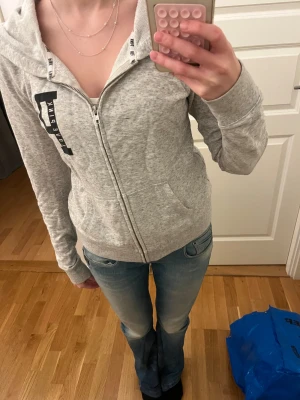 Grå hoodie från PINK Victoria's Secret - Mysig grå hoodie från PINK Victoria's Secret med svart tryck på bröstet och dragkedja framtill. Tröjan har huva med två fickor. Säljer då den inte kommer till användning 💗