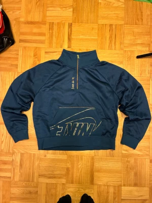 Marinblå Nike half zip sweatshirt S - Snygg marinblå sweatshirt från Nike med half zip och hög krage. Framsidan har stort Nike-tryck i guld och texten 'Just do it.' vid dragkedjan. Tröjan har en stor magficka och är tillverkad i mjuk fleece med långärmad passform. Perfekt för chill eller träning.