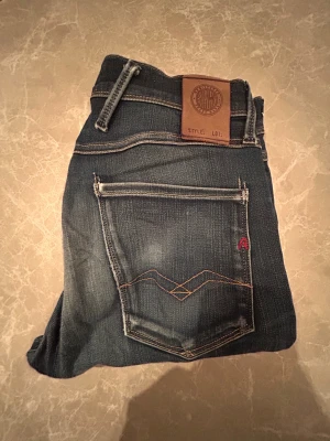 Replay Anbass jeans mörkblå - Snygga Replay Anbass jeans i mörkblå tvätt med slitningar och kontrastsömmar. Klassisk femficksmodell med läderpatch bak i midjan och diskret Replay-logga. Jeansen har rak passform och är tillverkade i stretchigt denim för extra komfort.