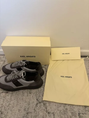 Axel Arigato Genesis Vintage skor - Snygga sneakers från Axel Arigato i grått och svart läder och mocka. Skorna har snörning och detaljer. Medföljer originalkartong och dustbag. Skorna är bara använda ett par gånger. Perfekt för dig som gillar stilrena och moderna sneakers.