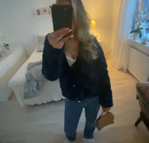 Svart pälsjacka från Vero Moda - Säljer en svart pälsjacka från Vero Moda med snyggt vågigt mönster i materialet. Jackan har rund hals, knappar framtill och långärmade ärmar. Perfekt för dig som vill ha en mysig och trendig look i höst och vinter.