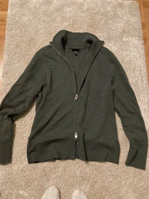 Mörkgrå kofta med dragkedja - Snygg mörkgrå kofta med hel dragkedja och hög krage. Tröjan är långärmad och har en stilren, enkel design som funkar till många olika looks. Materialet känns mjukt och är troligtvis bomull eller ullblandning. Perfekt för lager-på-lager under kyliga dagar.