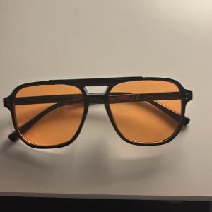 Orangea solglasögon  - Snygga solglasögon med svart pilotbåge och orangefärgade glas.  Perfekta för dig som vill ha en unik accessoar till din outfit.