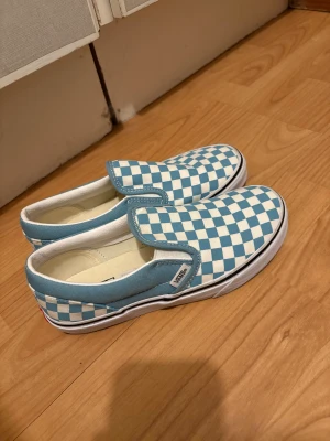 Vans slip-on blåvita rutig sneakers - Säljer ett par Vans slip-on sneakers i storlek 35 med klassiskt blåvitt rutigt mönster. Perfekt för dig som gillar streetstyle och vill sticka ut med en ikonisk look. Aldrig använda 