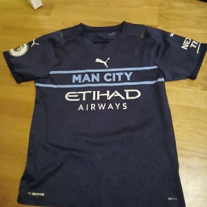 Manchester City Sterling #7 fotbollströja - Snygg mörkblå Manchester City matchtröja från Puma med tryck 'STERLING 7' på ryggen och officiella Premier League-märken på ärmarna. Framsidan har Man City-logga och Etihad Airways sponsortryck. Tillverkad i lätt polyester med DryCell-teknologi.