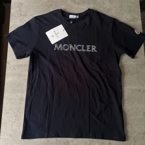 Svart Moncler t-shirt  - Hej, Säljer en svart Moncler T-shirt som är i Storlek L (Du kan skicka din vikt och längd så säger jag om det passar eller inte) 😊                           OBS!!! Der står XL men passar L (Tryckfel)
