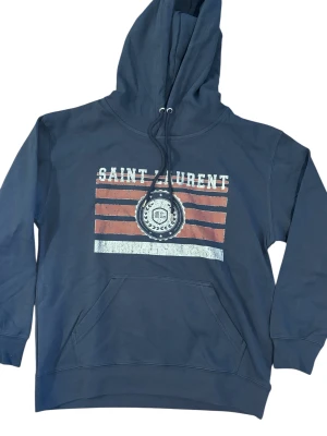 Mörkblå Saint Laurent hoodie - Snygg mörkblå hoodie från Saint Laurent med tryck på bröstet i rött, vitt och blått. Materialet är mjuk bomull och passformen är normal. Perfekt för dig som gillar streetwear och vill sticka ut.