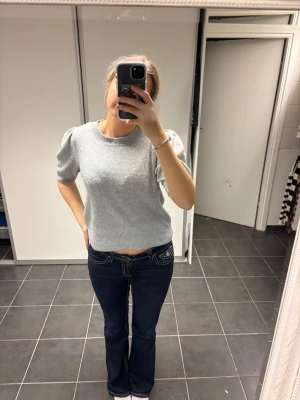 Grå stickad puffärm tröja - Snygg ljusgrå stickad tröja med puffärmar och rund hals. Kortare modell som sitter normalt och har ribbade muddar vid ärmslut och nederkant. Perfekt för dig som gillar stilrena och trendiga detaljer.