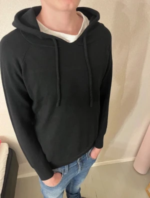 Svart hoodie med huva och snörning - Svart hoodie med klassisk huva och snörning framtill. Tröjan har långärmad design och en normal passform som sitter skönt. Perfekt att slänga på sig till jeans eller joggers. Materialet känns mjukt och bekvämt mot huden.