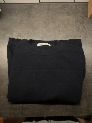 Mörkblå stickad tröja från Samsøe Samsøe - Snygg mörkblå stickad tröja från Samsøe Samsøe med rund hals och ribbade muddar. Enkel och stilren design som funkar till jeans eller chinos. Materialet är mjukt och värmande, perfekt för kyliga dagar. Passformen är normal och ärmarna är långa.