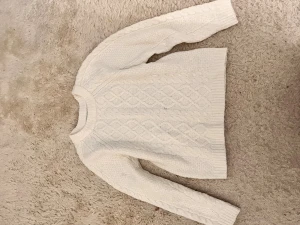 Vit stickad kabeltröja  - Säljer en vit stickad tröja med klassiskt kabelmönster och rund hals. Tröjan har långa ärmar och ribbade muddar vid hals, ärmslut och nederkant. Perfekt för dig som gillar mysiga och stilrena plagg med lite chunky känsla.