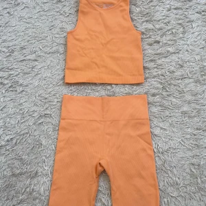 Ribbat träningssett - Säljer en ribbad orange träningssett från Primark. Toppen är ärmlös med rund halsringning och croppad passform med matchande shorts. Materialet är stretchigt och bekvämt med inslag av nylon och elastan.
