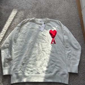 Vit stickad tröja från Ami med hjärta - Säljer en vit stickad tröja från Ami med rött hjärta och bokstaven A på bröstet. Tröjan har rund hals, ribbade muddar och lång ärm. Perfekt för dig som gillar stilrena plagg med en twist. Storlek XL men passar även L🤗Själv bär jag L och den är lite för stor för mig men inte alldeles för stor!😃