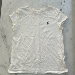 Vit t-shirt från Polo Ralph Lauren - Klassisk vit t-shirt från Polo Ralph Lauren med broderad marinblå logga på bröstet. T-shirten är i mjuk bomull, har rund hals och korta ärmar. Enkel och stilren modell som passar till allt. 